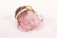 Newborn baby girl sleeps atop soft fuzzy white blanket during newborn photography session