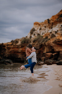 Couple playing in shallow water with cliffs behind them.
