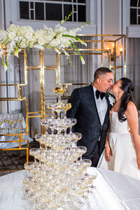 Bride and groom kiss next to a champagne tower at their wedding reception
