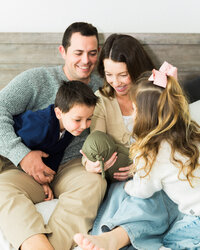 Parents and siblings gathered together around their newborn baby during an in-home lifestyle family photography session.