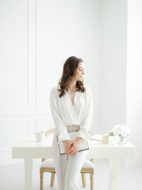 Photo of a business owner sitting on her desk holding her notebook as she looks down over her shoulder.