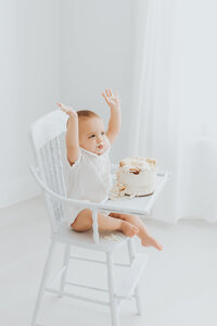 1 Year old baby boy in white outfit celebrates his first birthday with a cake smash photography session by Worth Capturing