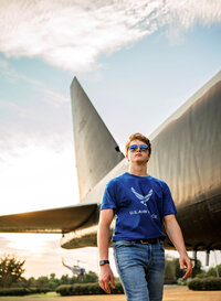 Senior portrait at Battleship Memorial Park in Mobile, Alabama— walking and wearing shades with a c-130 in the background.