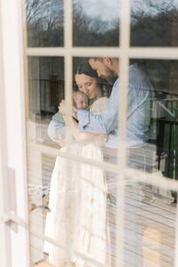 parents seen through door holding newborn son in at home newborn photos in peoria il