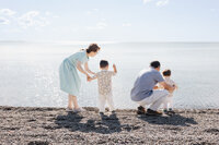 On a rocky Toronto Beach, a family of four, including two children and their doting grandparents, gather with sunlight dancing on the lake's surface—a perfect moment for Family Photography.