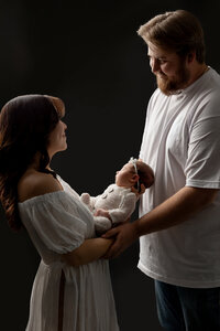 Parents smiling at each other while holding their newborn baby girl during a soft studio newborn family portrait by Kaitlyn Dawn Photography.