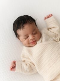 Sleeping newborn in a cream knit outfit during a studio newborn session.
