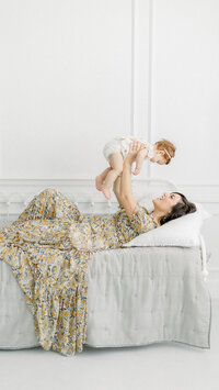 A in studio mommy and me session of a mother laying on a bed while she holds her baby up.