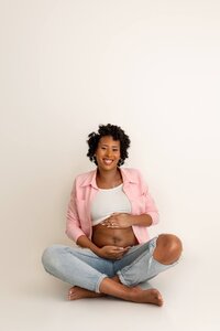 smiling pregnant mom seated holding baby bump in casual, classic studio maternity photoshoot