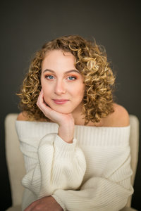 Teen girl with blonde curly hair poses for portrait in white sweater