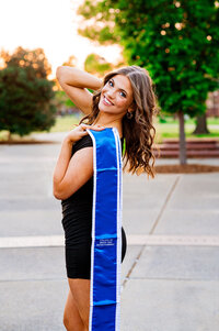 AOII MTSU college senior photo at golden hour, girl smiling over her shoulder wearing a blue stole
