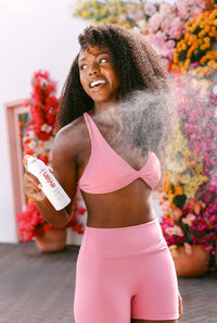 Model in pink activewear misting after a workout against a wall of flowers