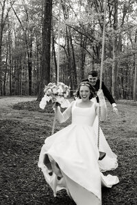 A whimsical black and white moment of a bride on a swing, preserving the atmosphere and emotion of an intentional outdoor celebration.