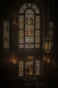 Vitraux historiques ornés de personnages médiévaux, boiseries sombres et lampe suspendue en fer forgé, détail architectural du Mount Stephen