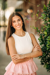 Senior portrait in downtown Foley, Alabama — waist-up with arms crossed and shop light bokeh
in the background.