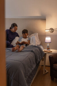 Mother and son reading together at bedtime, device charger on the nightstand