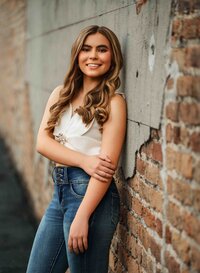Senior girl wearing jeans and a white tank top leaning against a brick wall in downtown Mobile, Alabama.