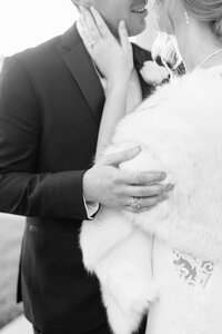 Bride in fur stole holds her groom's face on their wedding day