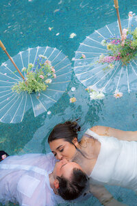 wedding couple kissing in pool with parasol umbrellas and flowers at rainbow oaks ranch in sanger california
