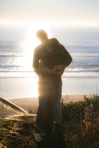 couple embracing in sunset ocean sparkle on cliffside in santa cruz