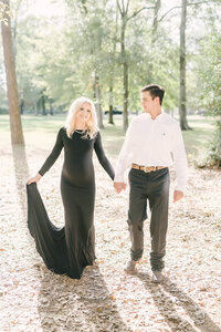 Husband and wife walk hand in hand through park during maternity session