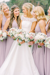Bride with bridesmaids in purple dresses holding white flower bouquets