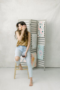 Professional headshot of a Fort Worth business owner sitting on a stool holding a glass of wine as she looks out of a window at a Dallas photography studio.