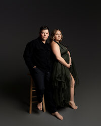 Expecting couple posing together during a studio maternity photoshoot by Kaitlyn Dawn Photography.