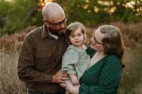 a couple kisses on their daughgter during their family photo session in frisco,texas.
