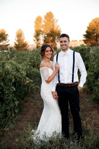 Newlywed couple standing together in vineyard at sunset