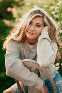 A female senior from Kettle Moraine High School sits in a backward, vintage dining chair among the wildflowers at Minooka Park in Waukesha.