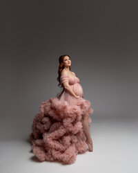 Side profile maternity portrait of an expecting mother in a blush pink ruffle gown captured during a studio maternity session by Kaitlyn Dawn Photography.