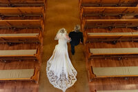 Top down balcony photo of a bride and her dad walking down the aisle in a Los Angeles church with warm yellow light.