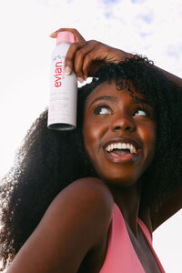 Close frame of a model applying Evian Glow facial mist to her hair, laughing