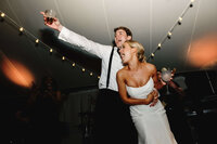 A high-energy documentary style wedding photography shot of a couple cheering on stage during dancing capturing the natural unfolding of a spirited reception.