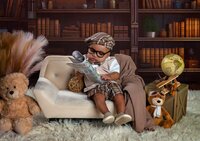 Baby boy wearing glasses and a plaid newsboy cap sitting on a small couch and holding a newspaper in a library-themed studio set during a child in Mandarin. - A portrait experience by Nature's Child Photography.