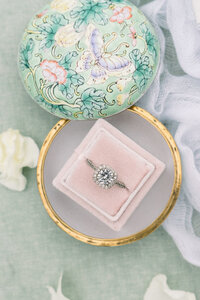 his exquisite detail shot by Tiffany Longeway features a stunning wedding ring nestled in a vintage pink ring box, symbolizing timeless love and elegance, and adding a touch of classic romance to the wedding narrative.