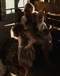 mother and three children sitting on a hay bail in a barn