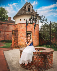 Young girl in blue and white dress seated on a brick wishing well at tryon palace