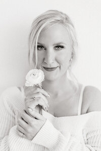 Black and white close up photo of a woman holding a fresh flower close to her face as her hair is falling in front of her face while she poses for her boudoir photos.