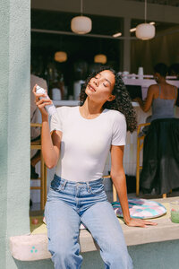 Model misting at a restaurant doorway in a white tee and denim