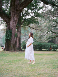 Wide shot of a barefoot pregnant woman surrounded by landscaping, looking in the distance
