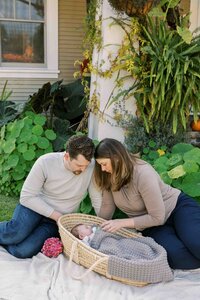 New parents sitting on the grass in front of their bungalow home in Palo Alto, looking at their new baby with love