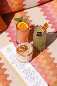 Three cocktails styled with a pool bar menu on a patterned textile