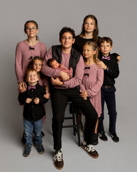 A portrait of five siblings and a sleeping newborn baby posed together in a studio during a professional newborn photography session in Yucaipa by Kaitlyn Dawn Photography.