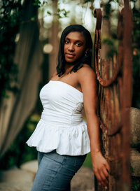 Senior portrait at Bella Sera Gardens in Loxley, Alabama — waist-up leaning back against a
rusted iron garden gate.