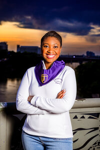 Senior girl smiling at camera at sunset wearing Lipscomb University jacket and graduating stole