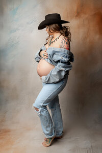 Pregnant woman wearing denim and a cowboy hat during a rustic styled studio maternity photography session by Kaitlyn Dawn Photography.