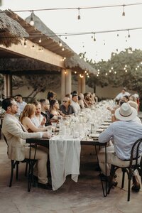 Guests sitting at a wedding table with white linens and bistro lights overhead