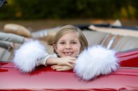 Jacksonville, FL portrait session capturing Joyful young girl in St. Johns, beams over the door of a bright red convertible, fluffy white sleeves framing her face during a festive outdoor portrait session.